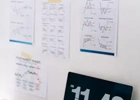 Office desk with financial charts on wall and a laptop displaying time, ideal for business themes.